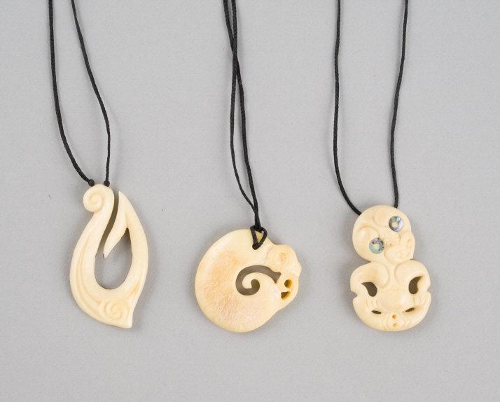 Maori Pendants, New Zealand: Three Maori Bone Tiki Pendants. New Zealand, mid to late 20th century, consisting of a Hei Tiki inset with natural material eyes measuring 2” long, one in the form of a fishhook measuring 2.25&r