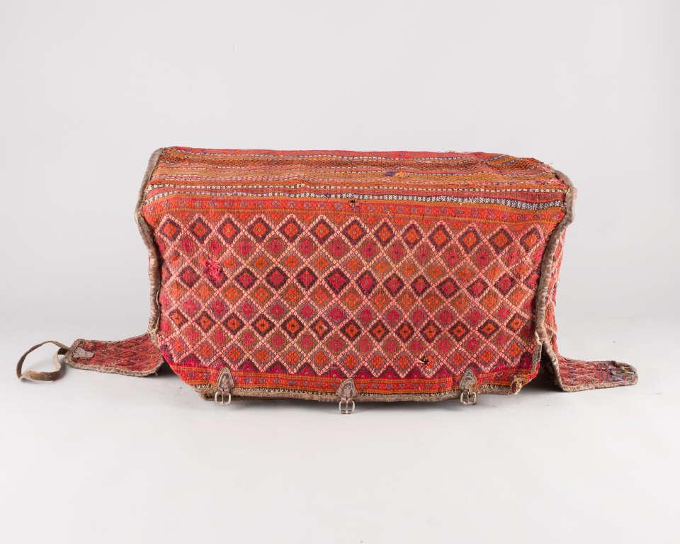 Persian Mafrash: An antique Persian Mafrash (bedding bag), woven with linear bands of geometric motifs and having leather carrying handles & straps, areas of wear, repair & losses, measuring 24" h x 44" w 20" d.