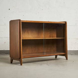 MCM WALNUT 'PROJECTION LINE' BOOKCASE BY DREXEL: USA circa 1950, showing a pair of glazed doors fronting a shelved interior, raised on arched stile supports. Measuring 31" high x 47" wide x 13" deep.