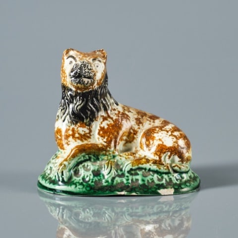 18TH C. STAFFORDSHIRE CREAMWARE LION: England circa 1790, the glazed hollow body moulded figure of a recumbent lion decorated with brown & black detail, atop a green painted naturalistic moulded base, (cracked & chip to base), measuring 3