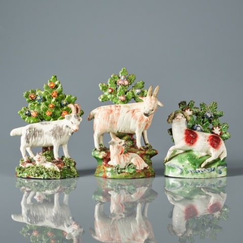 STAFFORDSHIRE PEARLWARE BOCAGE GROUPS: English circa 1845, two groups depicting rams with kids fronting flowering trees atop rocky mounds, one measuring 5.7/8" high, the other measuring 5.5/8" high, together with one of a reclining ewe mod