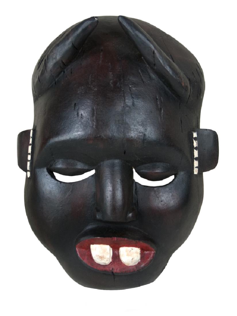 WOOD CARVED DAN MASK: This brown wood carved Dan mask is featured with a pair of devil horns on the top, a high forehead, a pair of deep eyes with slender gaps, a flat nose, and a wide open mouth painted in red with two bi