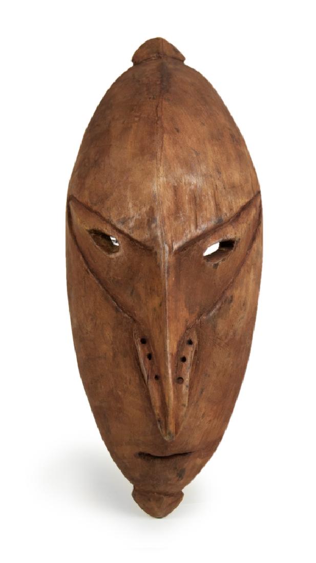 CARVED WOOD MASK: This wooden figure is carved in an oval form, with pointed ends, featured with a ridged line that divides the mask from top to the nose, a pair of oval eyes and three holes on each side of the sharp n