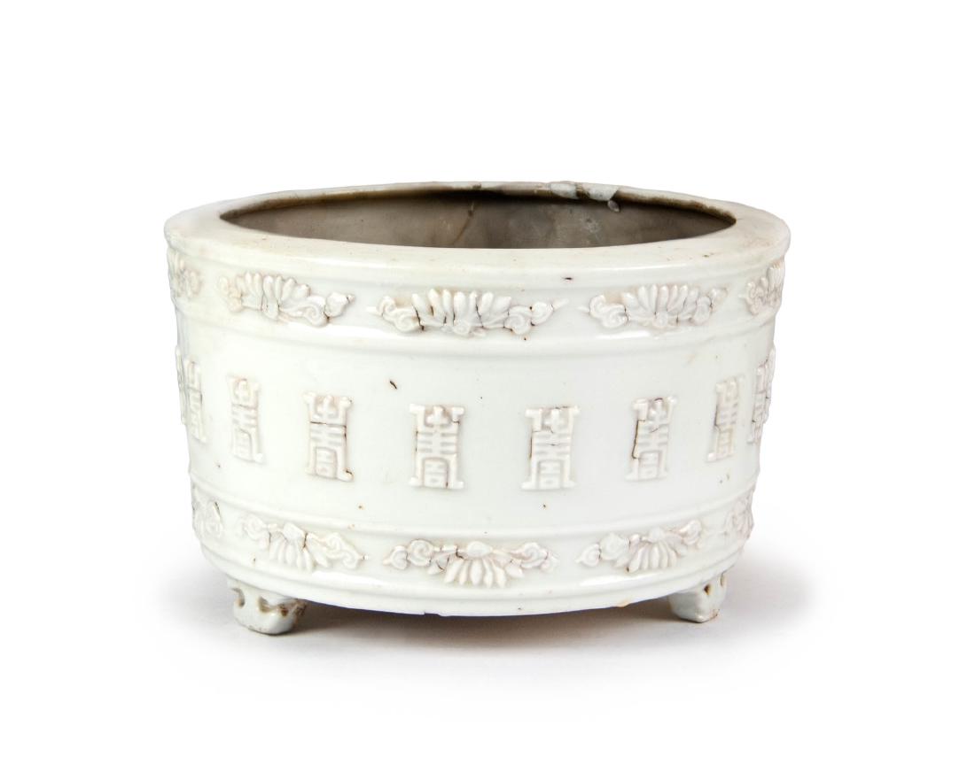 BLANC DE CHINE LONGEVITY CENSER: A circular Blanc de Chine tripod censer covered with shallow relief molds of Longevity symbols, lotus motifs along the top and bottom rims. H:3 1/4in(8.1cm) D:5 3/8in(14.6cm)