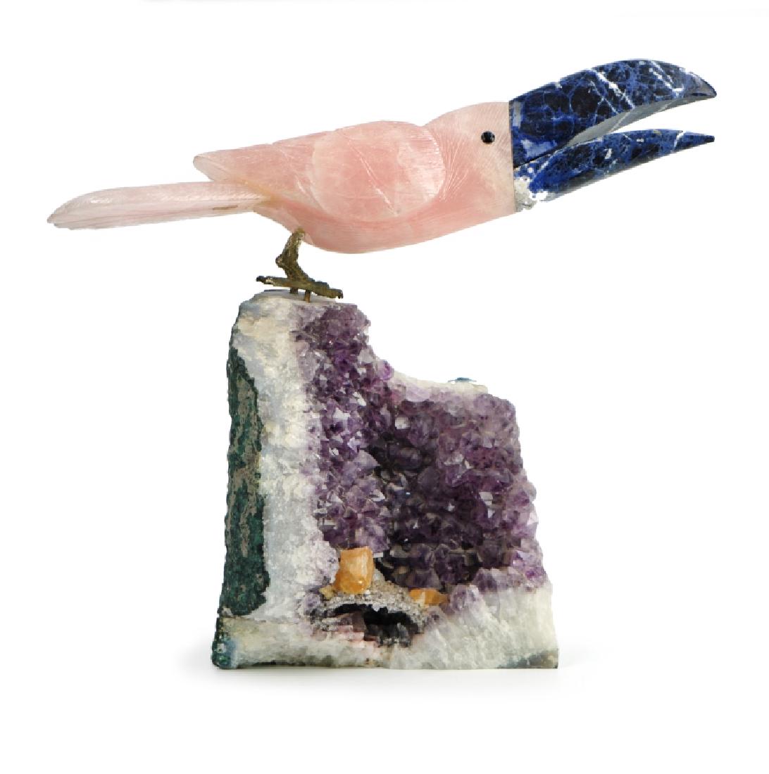 STONE CARVED TUCAN: Sitting on a geode of Amathist, the bird is rose quartz and his beak is lapis lazuli. 8 5/8in X 14 1/2in(22cm X 37cm)