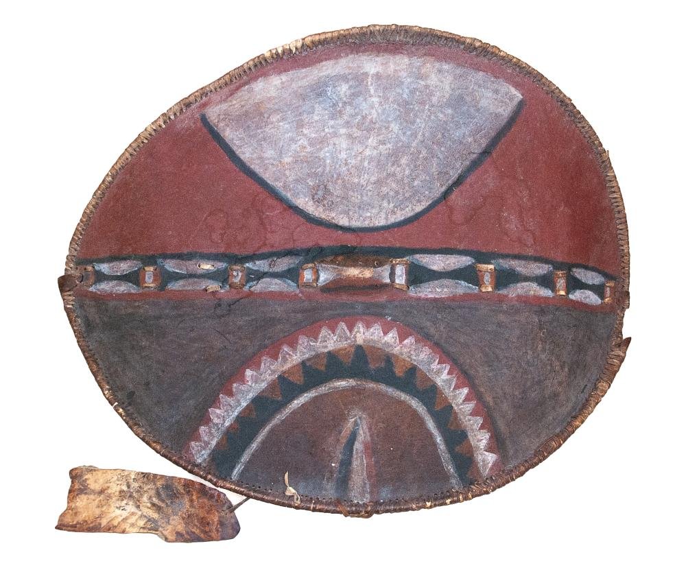 19TH-20TH CENTURY MASIA SHIELD: A shield in animal hide fabrication. This is a Masai shield from Africa. Its wooden backing bar is strapped to the center of the shield face with leather strips that show up 9 times down the center of