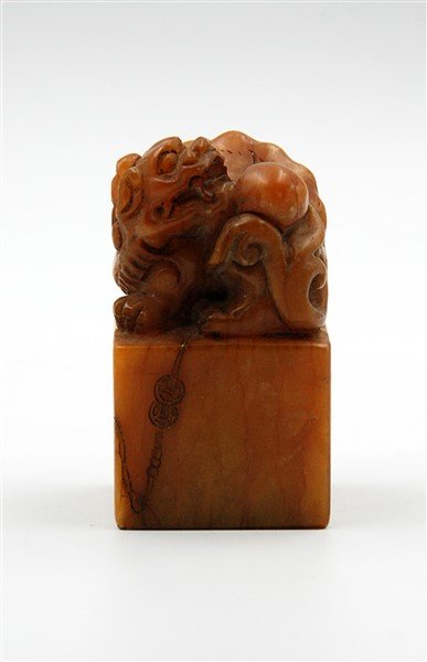 SOAPSTONE SEAL: Topped with a mythical creature, this amber colored stone seal has a signature carved on the bottom, and an inscription on one of the faces.L: 2 W: 2 H: 3.6 W: 16.8 oz