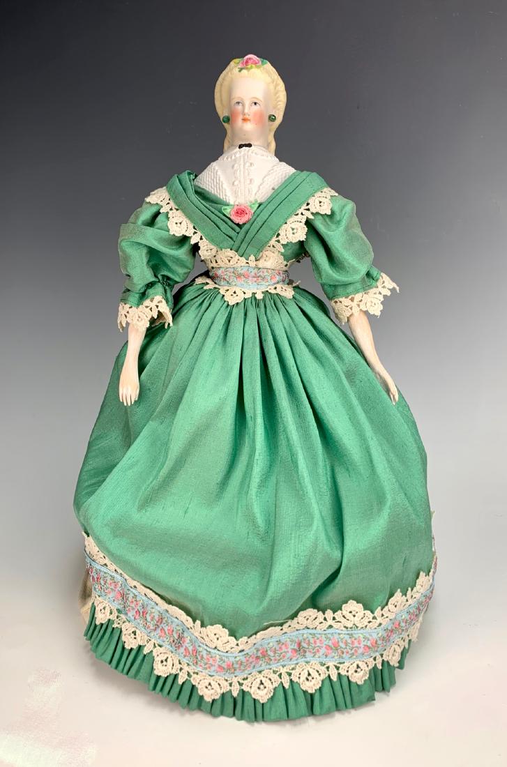 German Parian Shoulder Head C. 1860's: Light blue painted eyes, decorated blouse with black bow, pierced ears, fancy braided hairdo with molded black bow in back and rose on top, pierced ears, old cloth body, wooden forearms, shoulder plat