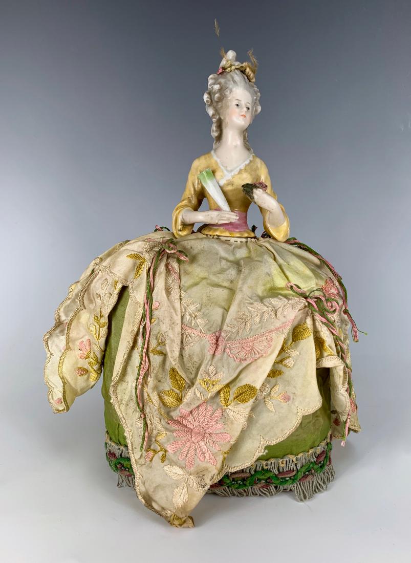 11" German Pin Cushion Doll C. 1920's: China head depicting Marie Antoinette, one hand away, all fingers repaired on left hand and unpainted, original silk embroidered clothes over a stuffed base, good condition, 11"