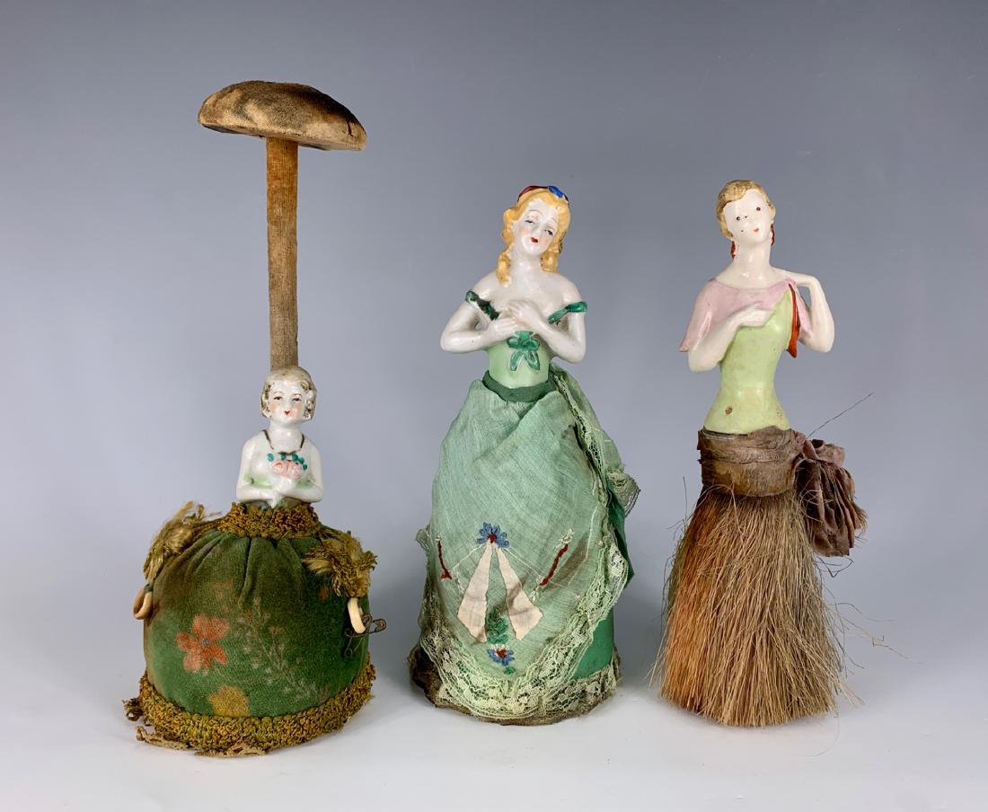 3 Pieces of Porcelain China Pin Cushions: One possibly in original costume in overstuffed base, 8"; one doll/hat stand, overstuffed base, original velvet costume, 10"; one doll brush, 8.25", all German and c. 1920's, all with some fire damage