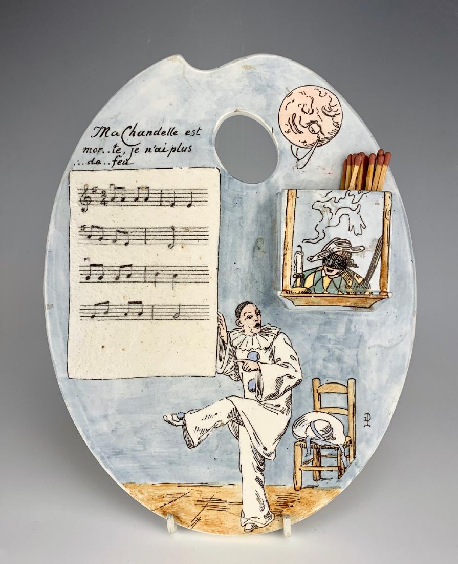 Signed Amusing Porcelain Wall Match Holder: Having the shape of an artist's palette, depicting a sheet of music with saying in French "My candle is dead, no more fire.", attached match holder, artist's initials signed on lower left, made by Kel