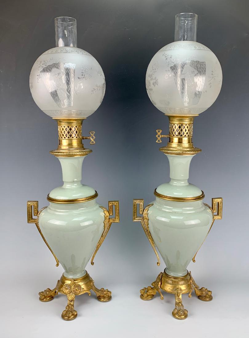 Pair Celadon & Bronze Oil Lamps Late 19th Century: Circa 1870, both lamps are celadon porcelain, having bronze mounts with eagle claw feet, each ball shade is white frosted decorated with Asian scenes of a lady under a parasol, birds and open fan, was