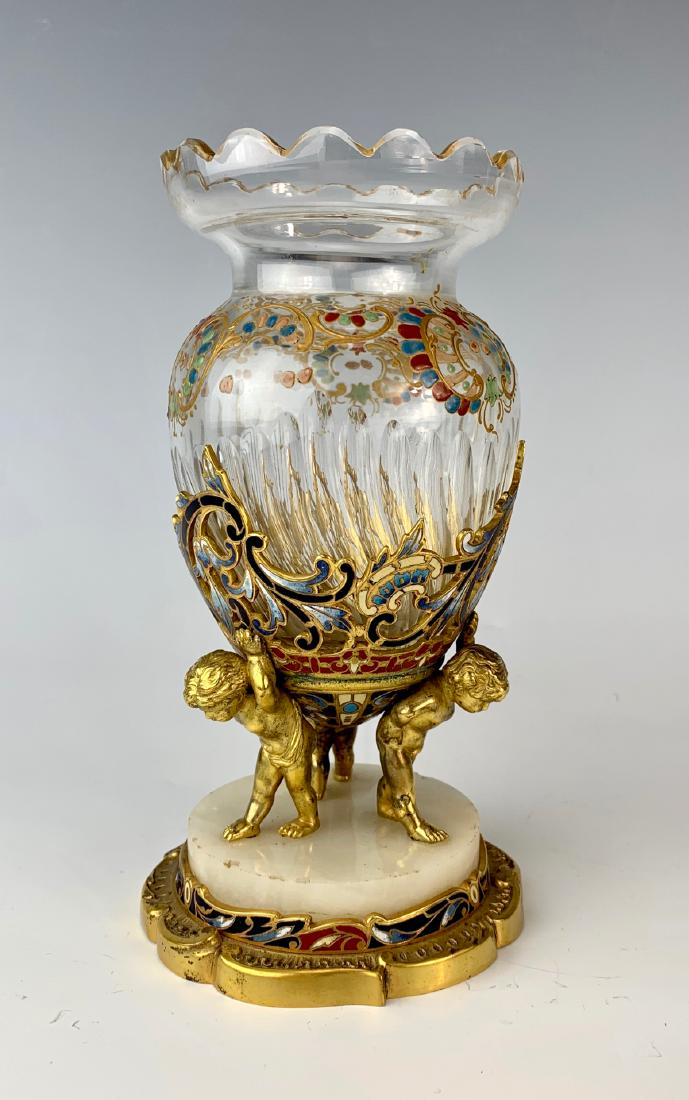 Gilt Bronze Putti Glass and Champleve Vase: Clear glass ribbed body encased in gilt bronze and champleve enamel, held up by 3 putti, base is onyx and enameled bronze, very good condition, 7" height**NOTE: Unfortunately, a chip has been discover