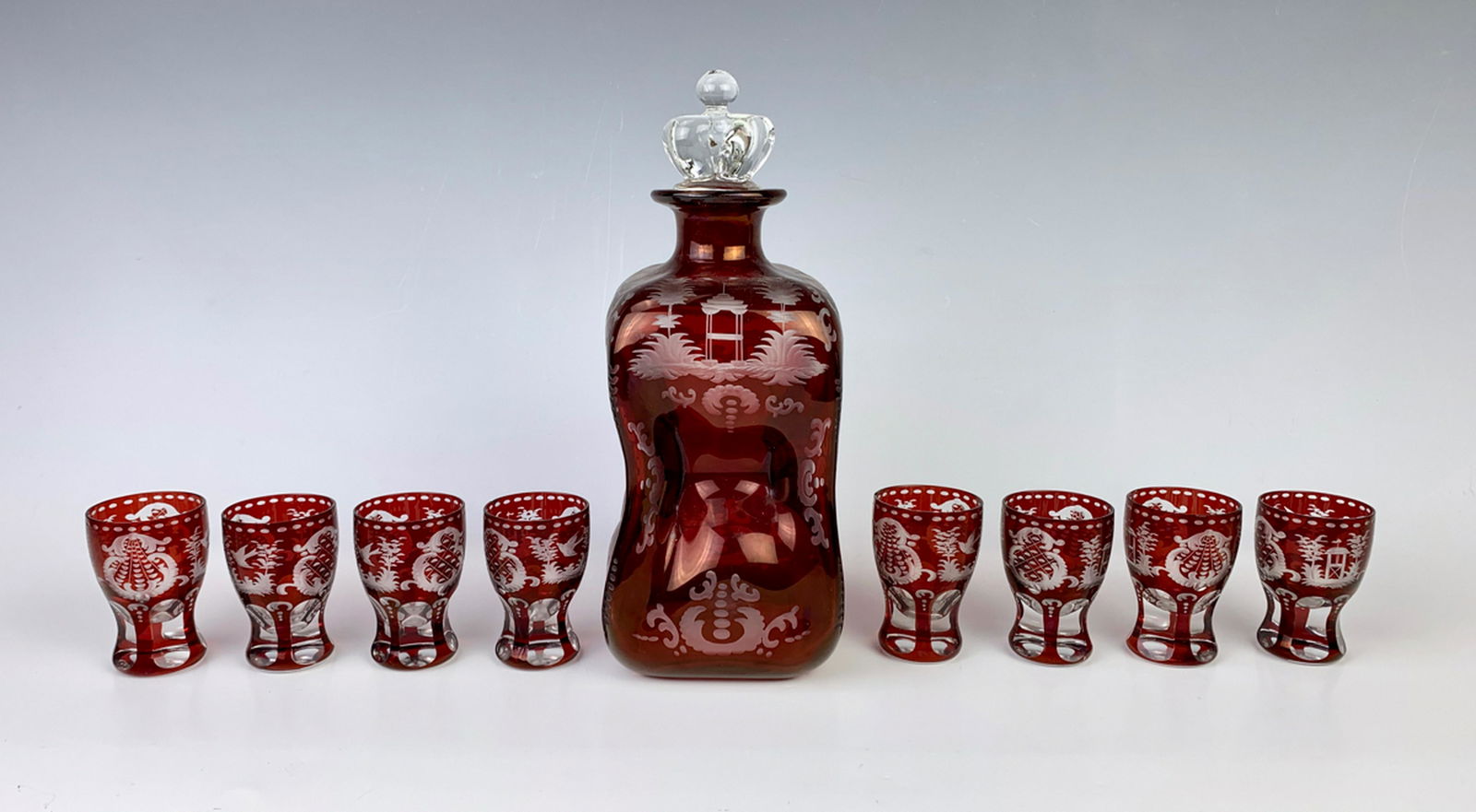 Ruby Red Bohemian Decanter & 8 Glass Liquor Set: Circa 1900, a decanter and 8 glasses, rich ruby flash over a clear body, decorated with cut scenes with birds and foliage and decorative scrolling designs overall, all in very good condition, decanter