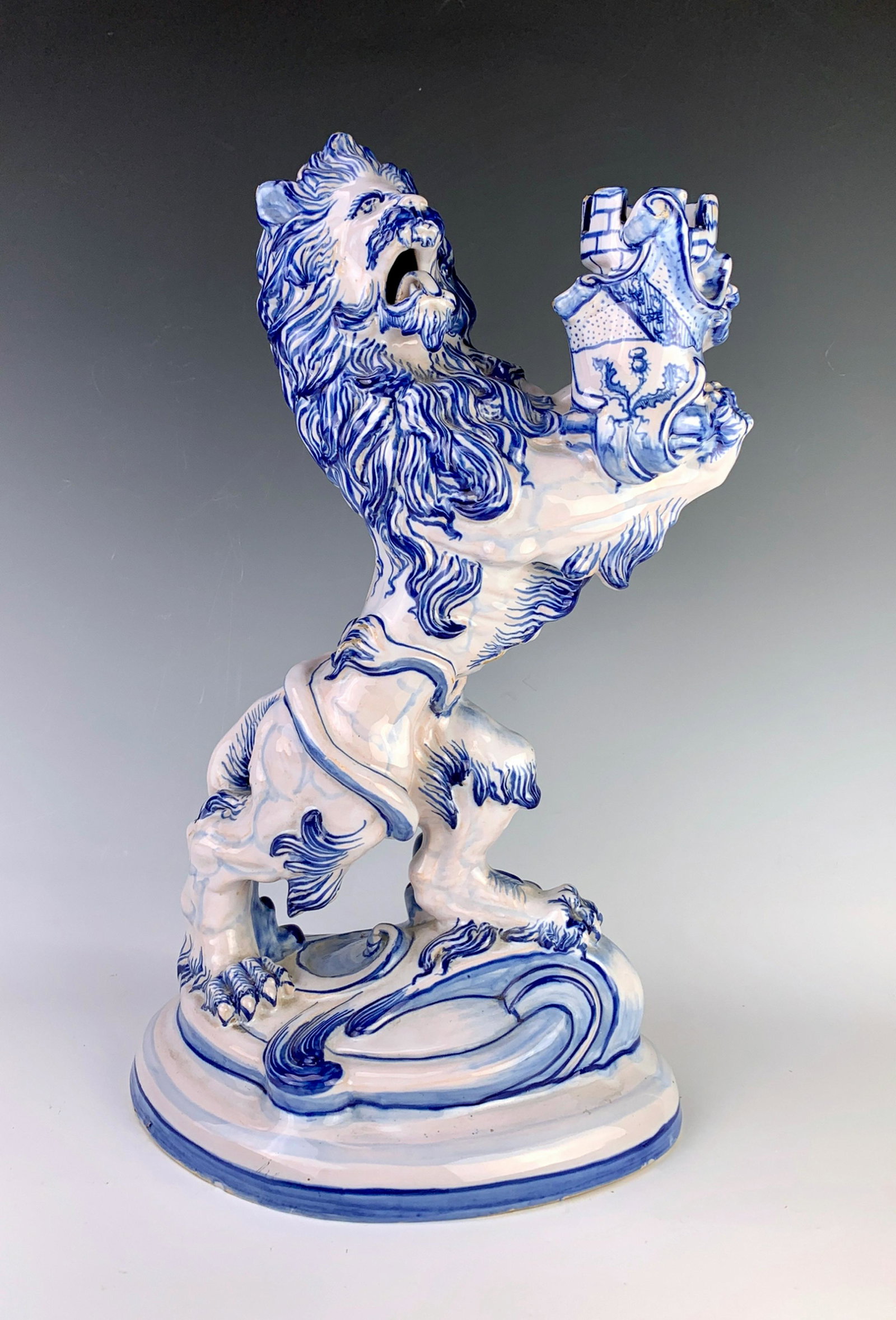 Signed Galle Pottery Lion Candlestick C. 1900: Depicting a standing lion holding a candle holder in a blue paint over a white glazed faience body, marked "Galle, Nancy Editeurs, St. Clement, Lorraine", good condition, 16.375" x 10.75" x 7.5"