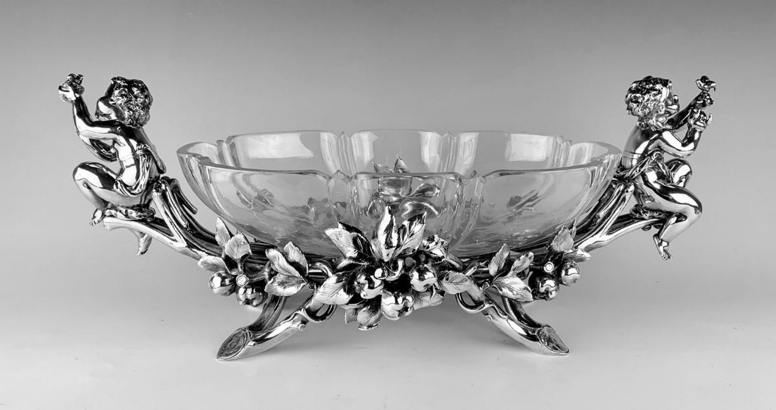 Christofle Silvered Bronze & Glass Centerpiece: Beautiful Christofle figural centerpiece, crafted of silvered bronze with seated putti flanking the oblong fruiting apple branch form body, each figurine is holding a bird in their hands, raised on fo