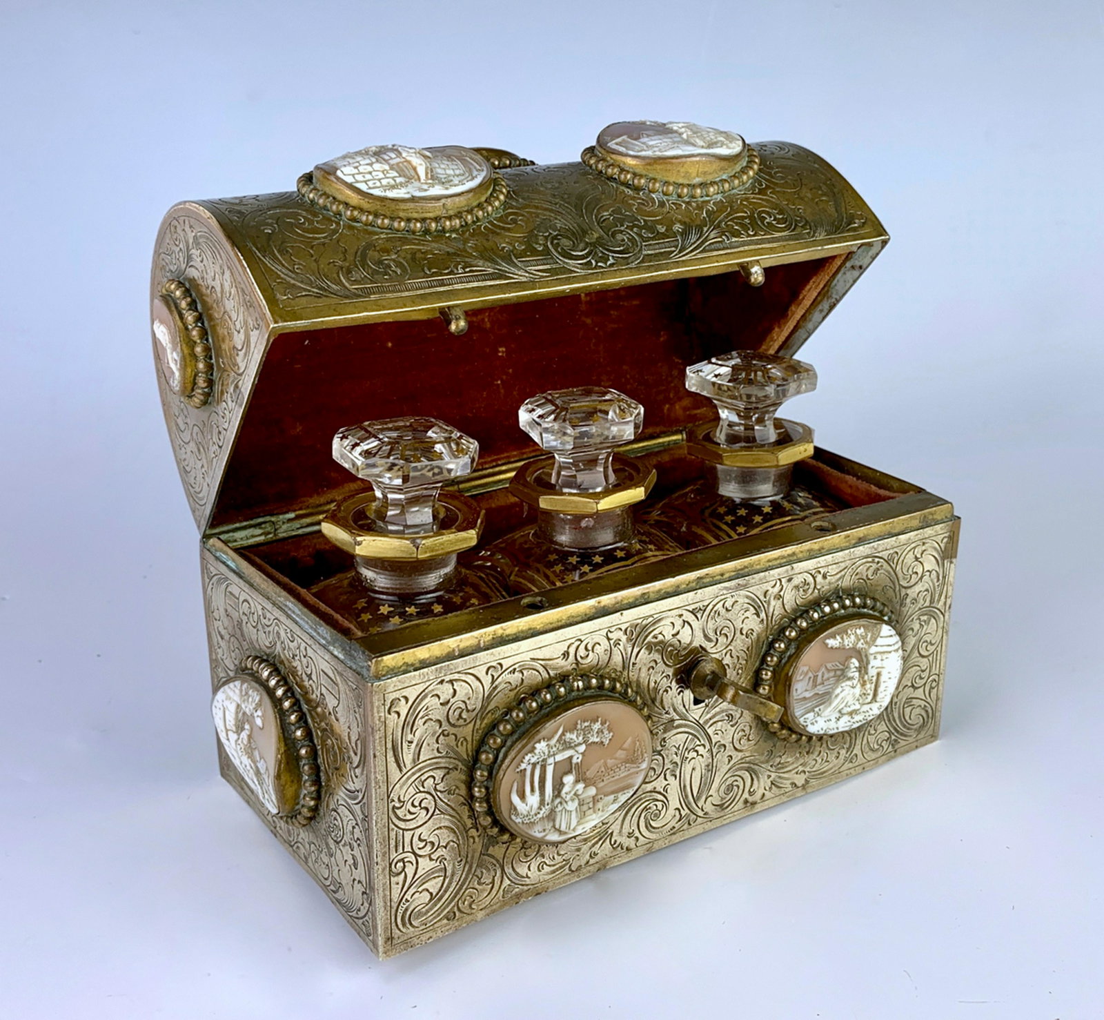 Antique Gilt Brass w/ 13 Cameo Perfume Casket: Circa 1880, has 3 crystal glass bottles with gold gilt and stoppers, mounted in red velvet holder, ornate etched brass casket and embedded with 13 scenic cameo shells, has original key and locks, good