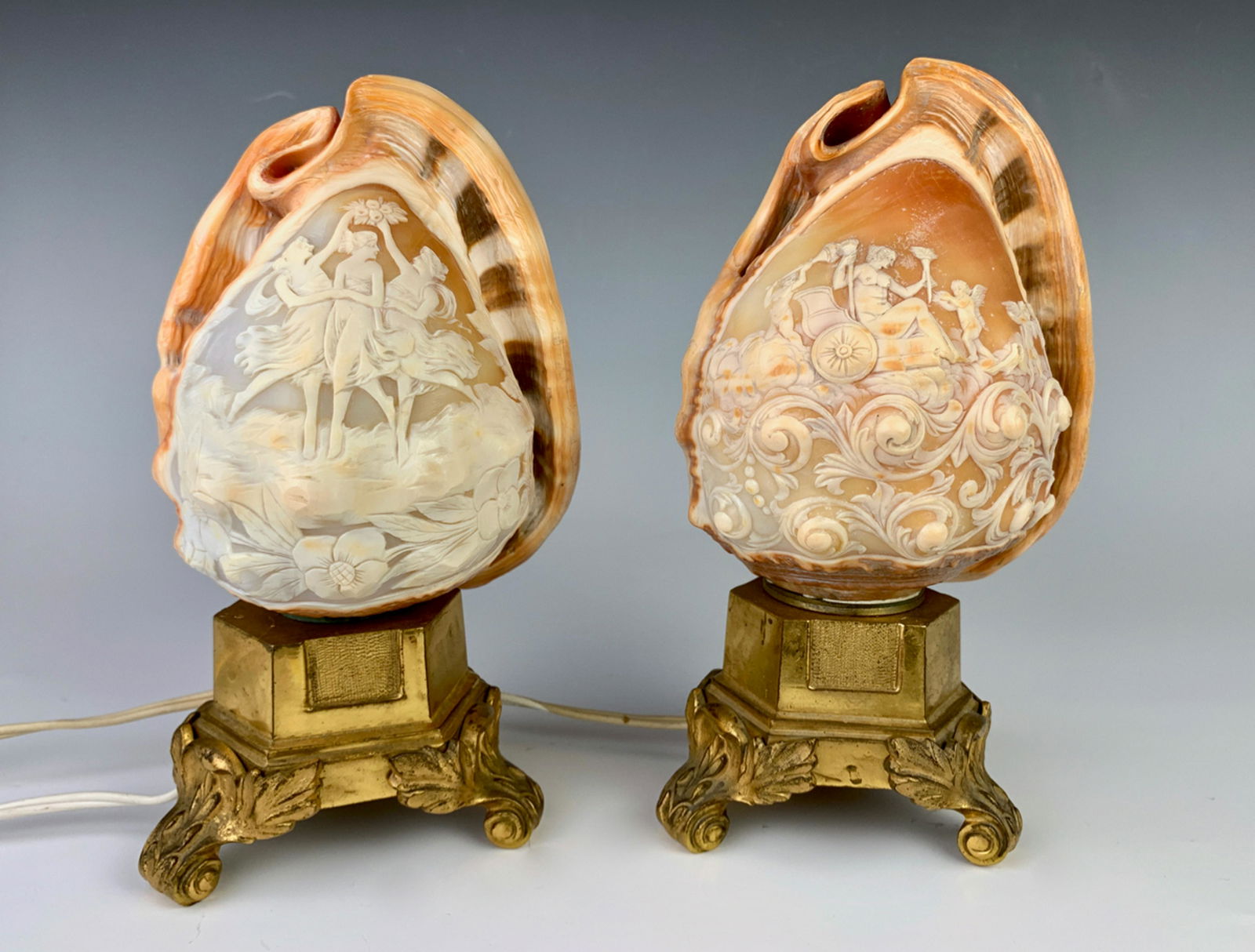 2 Italian Carved Shell Lamps w/ Gilt Bronze Bases: Circa 1900, superb pair of quality cameo shell carved lamps mounted on gilt bronze bases, one depicts the 3 Graces and the other a scene of cherubs and chariot, very good condition, 9" height