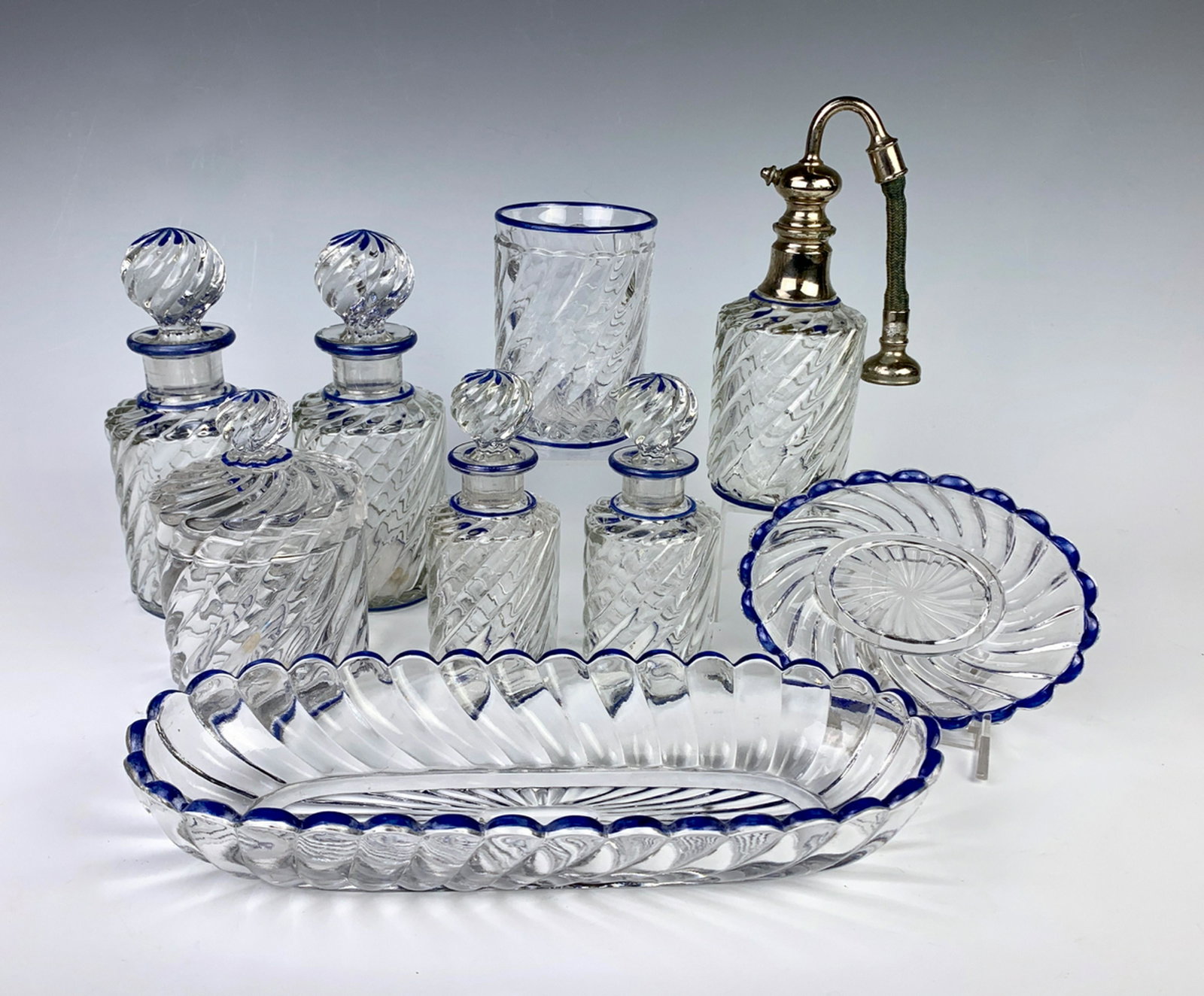 9 Piece Signed Baccarat Crystal Vanity Set: Circa 1920, made in France, 9 piece clear crystal twist design with blue enamel trim, 2 bottles signed with original Baccarat paper label, consisting of 4 bottles, atomizer, covered jar, toothbrush ho