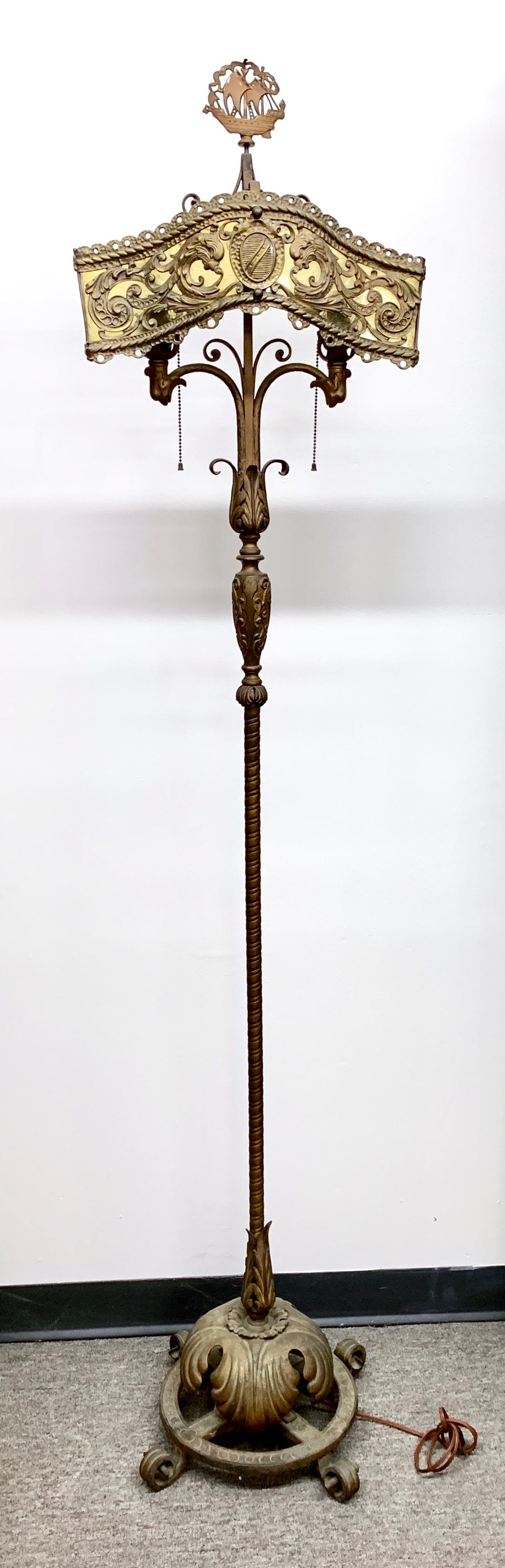 Oscar Bach Segar Studios Torchere Floor Lamp: From the early 20th century, bronze and iron metal base, shade is shaped horizontal ornate design with a clear amber glass panel and double socket not marked, has the Segar Studios ship finial, good c