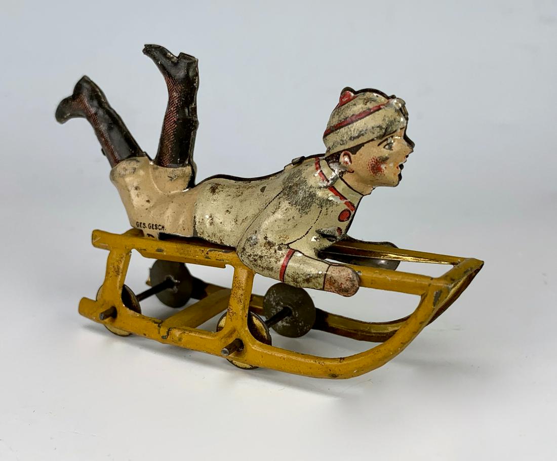 Antique German Tin Litho Boy on Sled Penny Toy: Marked "Gesch" on boy's pants, full bodied figure embossed lithographed tin penny toy, very good condition, 2" height **Lifetime estate collection of Jeannine Hamilton, Oak Park, CA** *Domestic in-hou