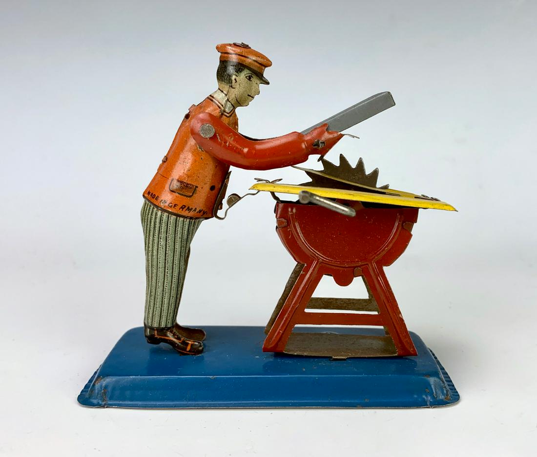 Antique German Tin Penny Toy "Man w/ Buzz Saw": Early tin embossed lithographed penny toy depicting a man and his buzz saw, works moving handle, very good condition **Lifetime estate collection of Jeannine Hamilton, Oak Park, CA** *Domestic in-hous