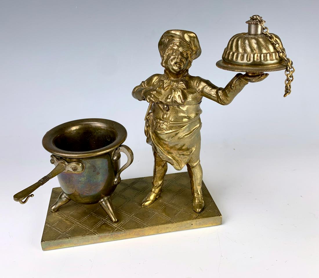 The Baker Bronze Cigar Lighter: Circa 1900, figural cigar lighter modeled as a baker with his tray (lighter) standing next to a handled cauldron which holds cigars, hinged torso reveals receptacle, nice patina, very good condition, 