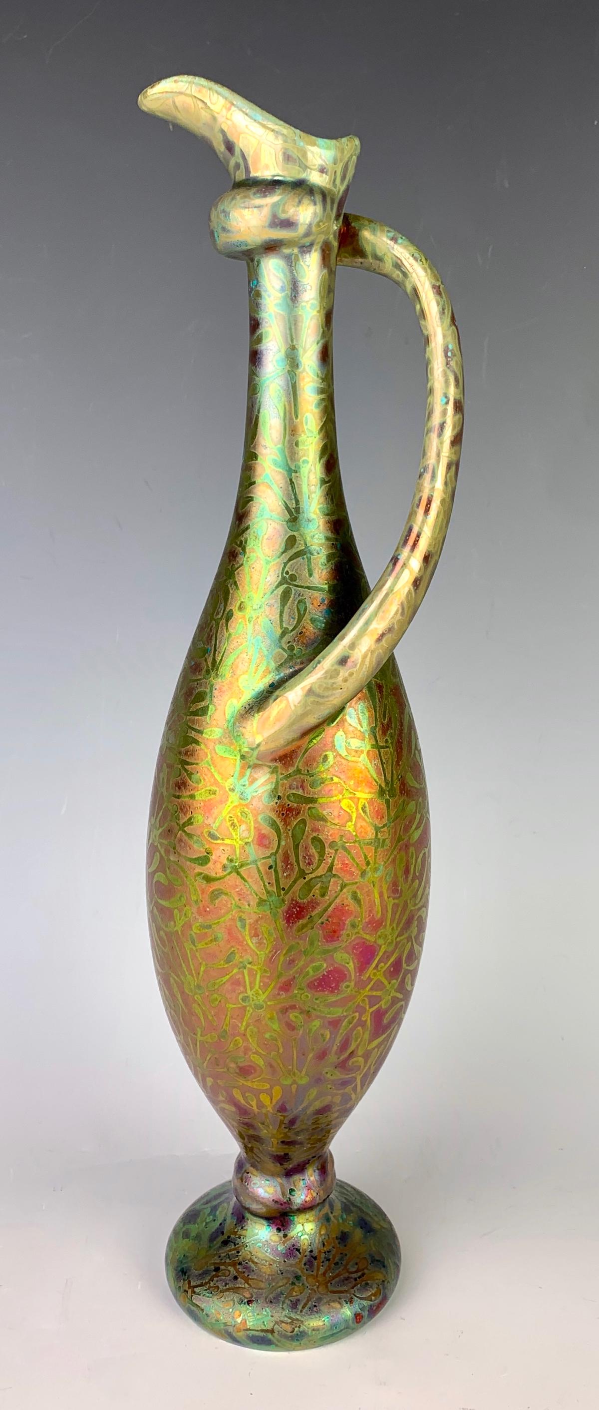 Signed Clement Massier (1844-1917) Vase: Having a bulbous body tapering to a narrow neck and having a twist handle, decorated with leaves and berries in red and green iridescence, signed on bottom "Clement Massier, Golf Juan Am", very good c