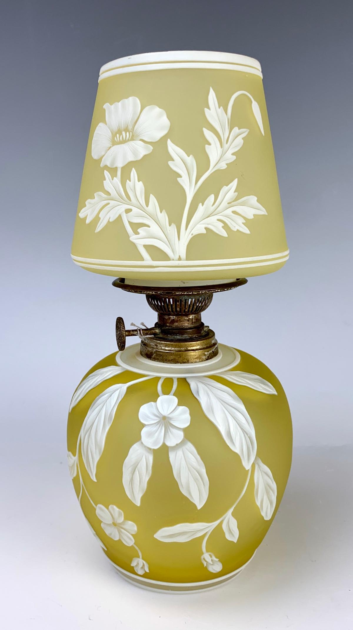 Webb English Cameo Lamp: Having a yellow satin body with white carved scenes of flowers, leaves and a butterfly, has original Thomas Webb & Sons paper sticker on bottom, the metal kerosene adjustment signed "The Silver Light 