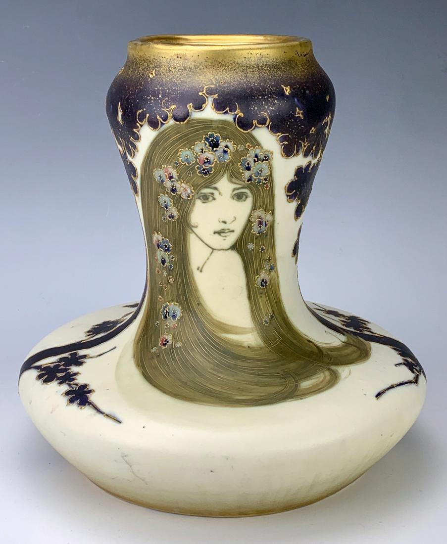 Amphora Portrait Vase: Circa 1890, the flared ivory porcelain body tapering to cylindrical top with hand painted portrait of a pretty woman, flowers adorn her hair, the top and back of vase, all with gilt accents, marked wi