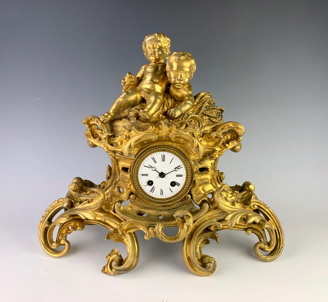 French Dore Bronze 2 Putti Clock C. 1880: Depicting two putti sitting atop an ornate gilt bronze case, has French movement with pendulum and key, good condition, dial has chipping around key hole, 15" x 17" *All clocks are sold as is and are 