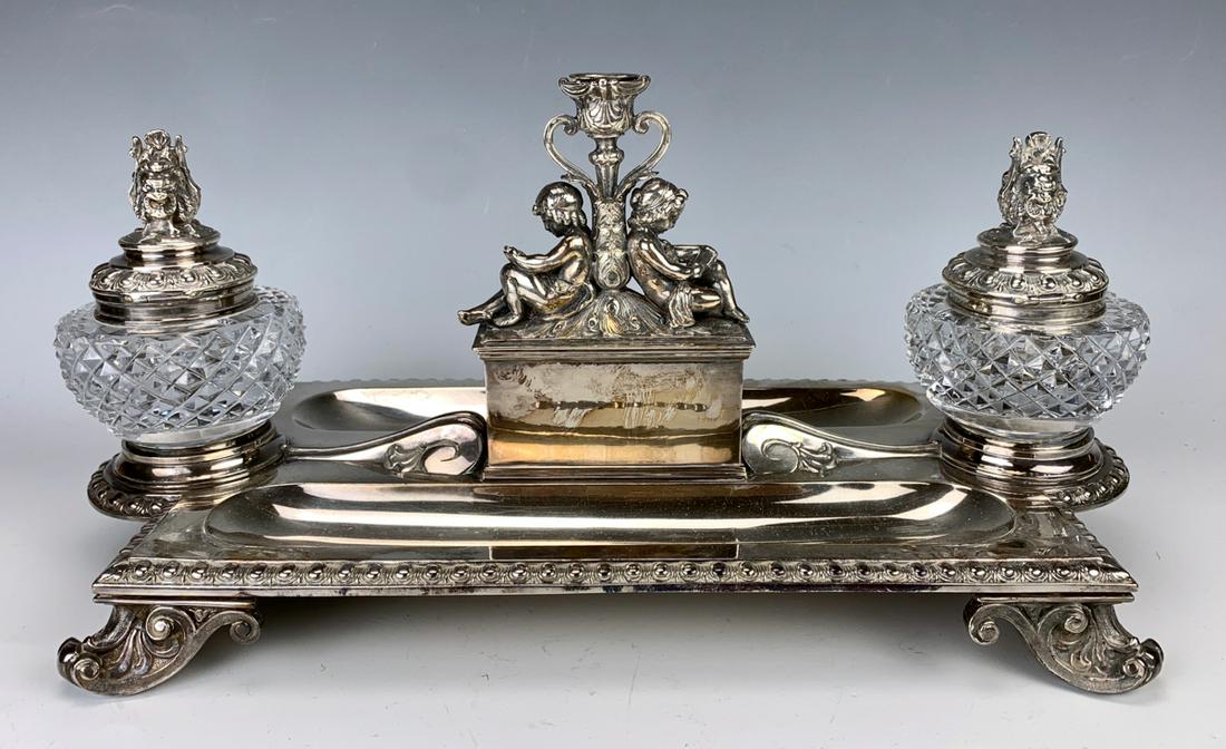 Elkington Figurel Silver Plate Inkwell C. 1900: Silver plate double inkwell with 2 crystal wells, having comedy and tragedy silver plate mask lids, also a back to back figural child supporting a candlestick, double pen tray, good condition, 7" x 14