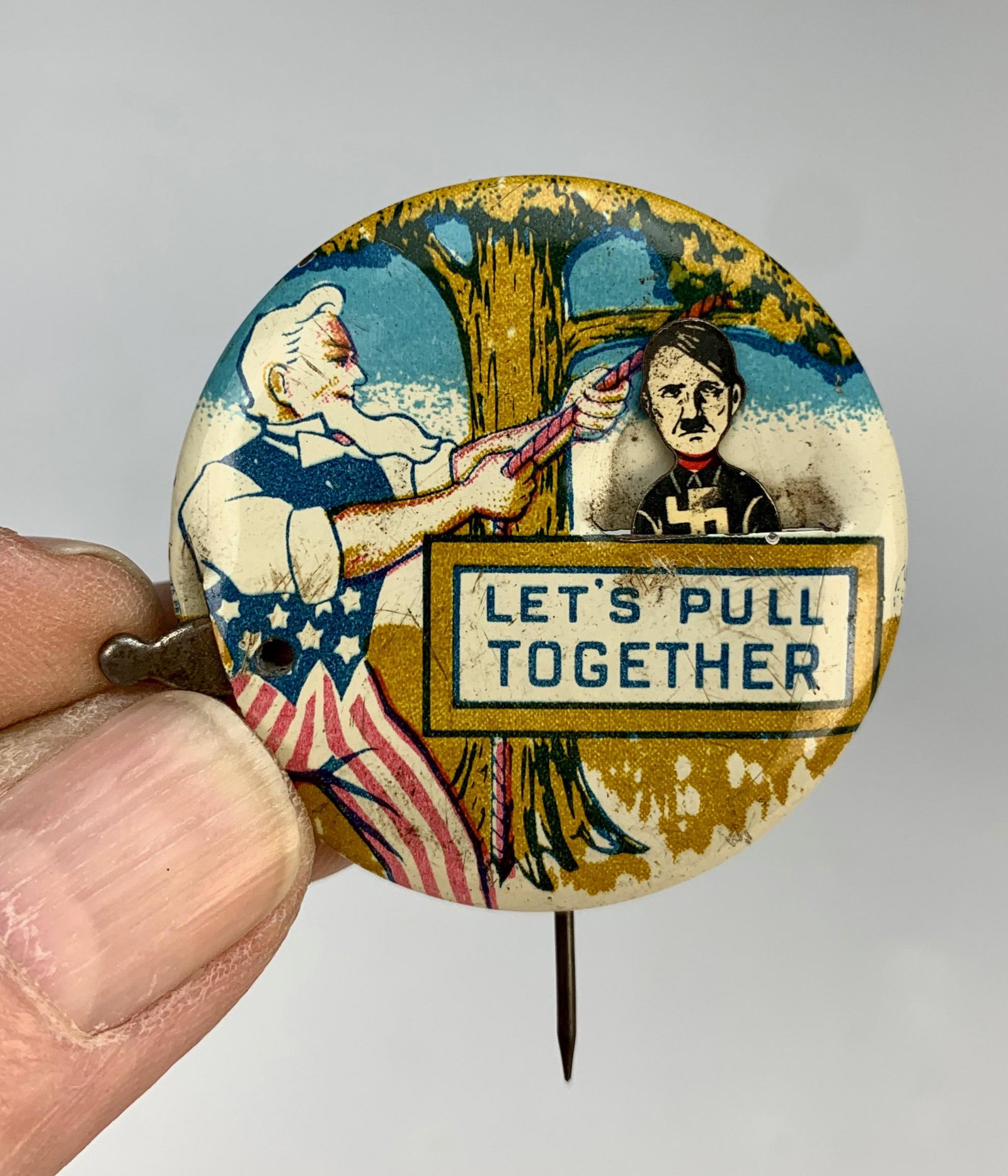 Uncle Sam "Let's Pull Back Together" WW II Pinback: Mechanical WW II pin showing uncle Sam lynching Hitler. Very good condition. 1.75" diameter.