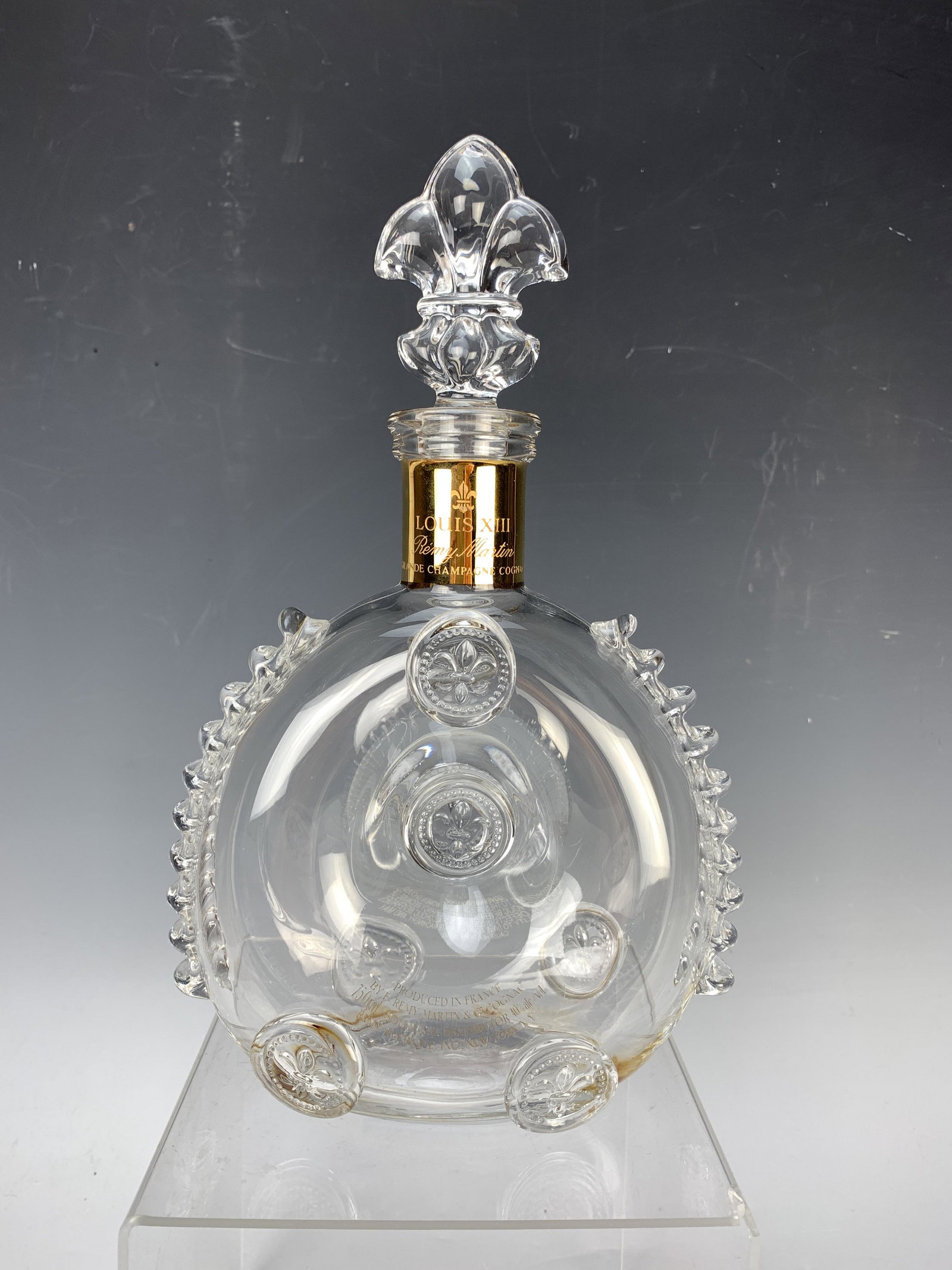 Baccarat Remy Martin Louis XIII Cognac Decanter: Crystal decanter with fleur de lis stopper and golden sleeve around the neck. Measures 11" high and weighs 1065 grams. Signed with both Baccarat logo and Artist's initials. Stopper and bottle have sam