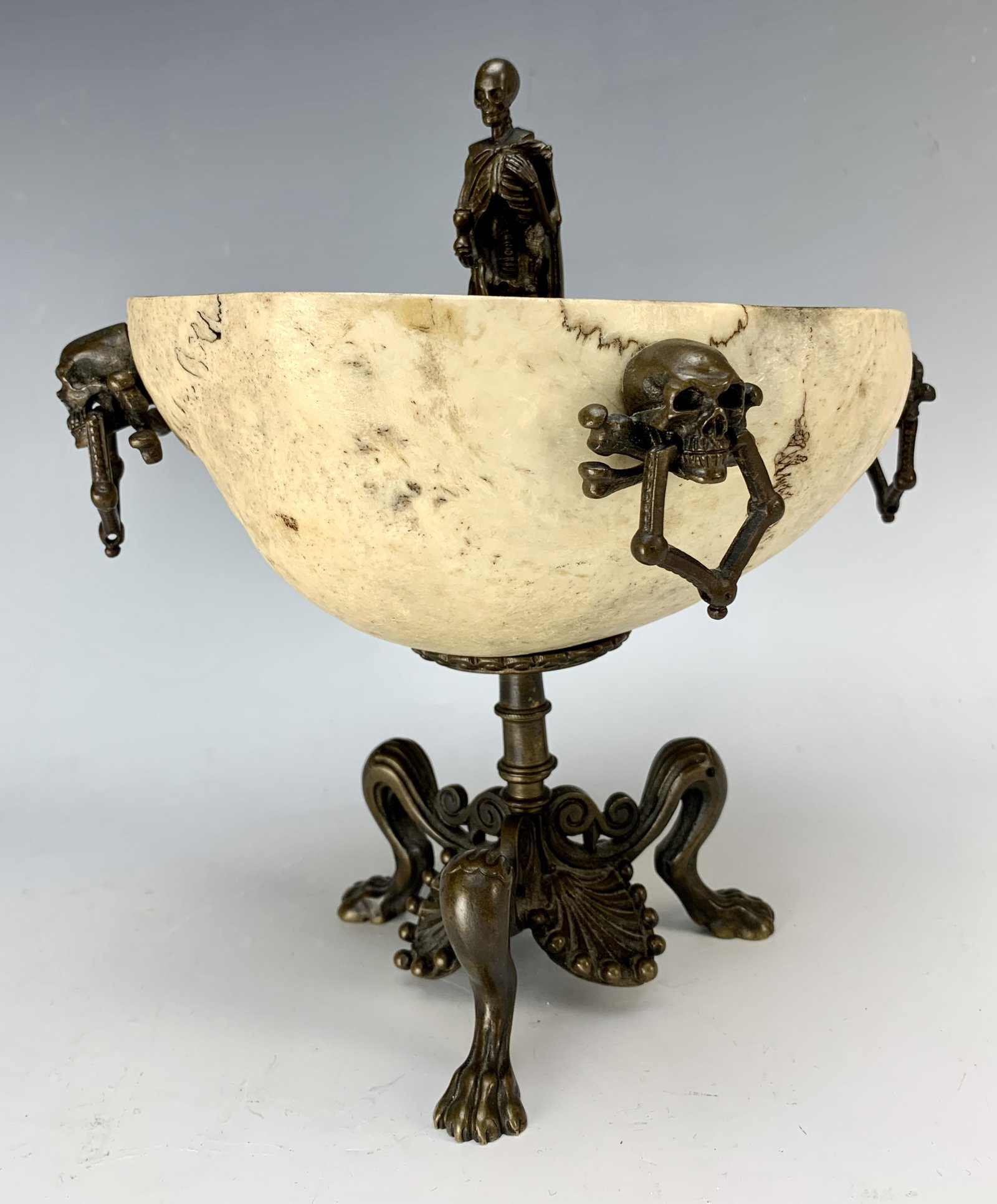 Bone Liberation Cup with Bronze Skulls & Skeleton: Early 19th Century most unusual curiosity. A bone skull cap with tripod bronze mount with paw feet and 3 skull and cross bone handles, surmounted by a skeleton holding an hourglass,8.5" tall, missing 
