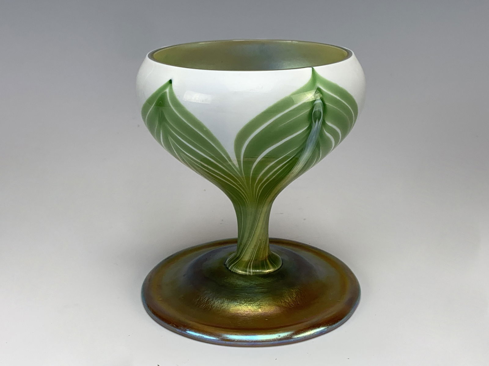 Tiffany Favrile Feathered Art Glass Goblet Sgd: A Tiffany iridescent feathered goblet with gold favrile base and body with green feathering over white and a gold interior, signed "L C Tiffany Favrile 8450 E", very good condition, 4" x 3".Have a sim