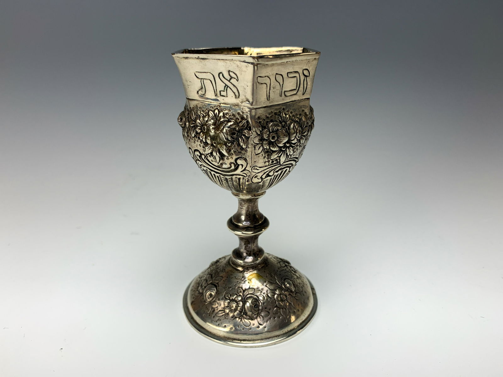 German Antique Hexagonal 800 Silver Kiddush Cup: This cup measures 4 3/4" high x 2 3/4" at the base and weighs 166 grams. Has a flower motif on the bowl and the prayer around the rim says to "keep the Sabbath holy". It is hallmarked on the bottom ed