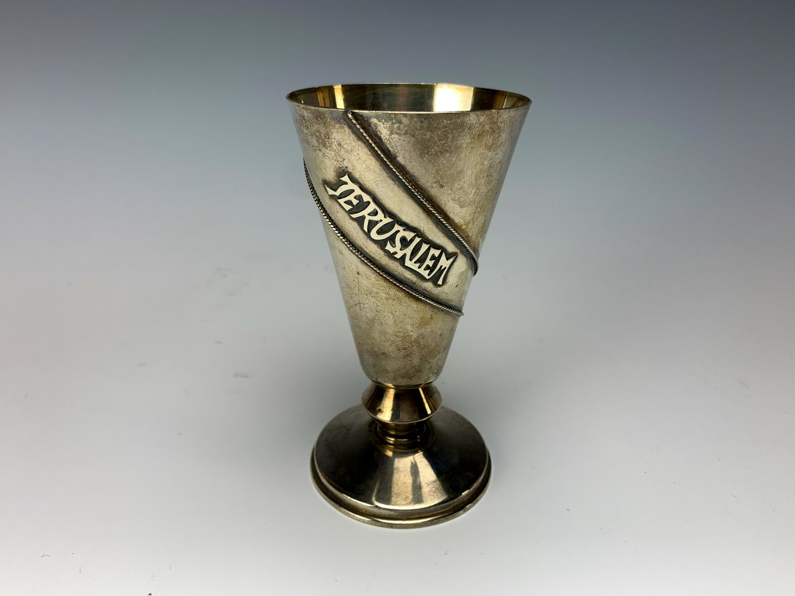 Dugma Sterling Silver Kiddush Cup: This cup measures 4 1/2" high by 2 1/4" wide and marked with the maker on the bottom edge. Sits flat on the table. JerusalemÃ­ is applied between the lines outside. Shows wear from age use and needs