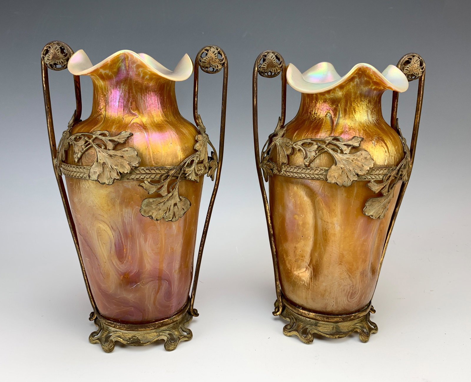 Pair Matched Of Loetz Type Glass & Bronze Frame: Great pair of Loetz-type gold with a touch of red iridescent vases encased in bronze ginkgo leaf decorated handled vases from the Art Nouveau period. C.1900" Size: 9.75" tall (each). Condition: Very g