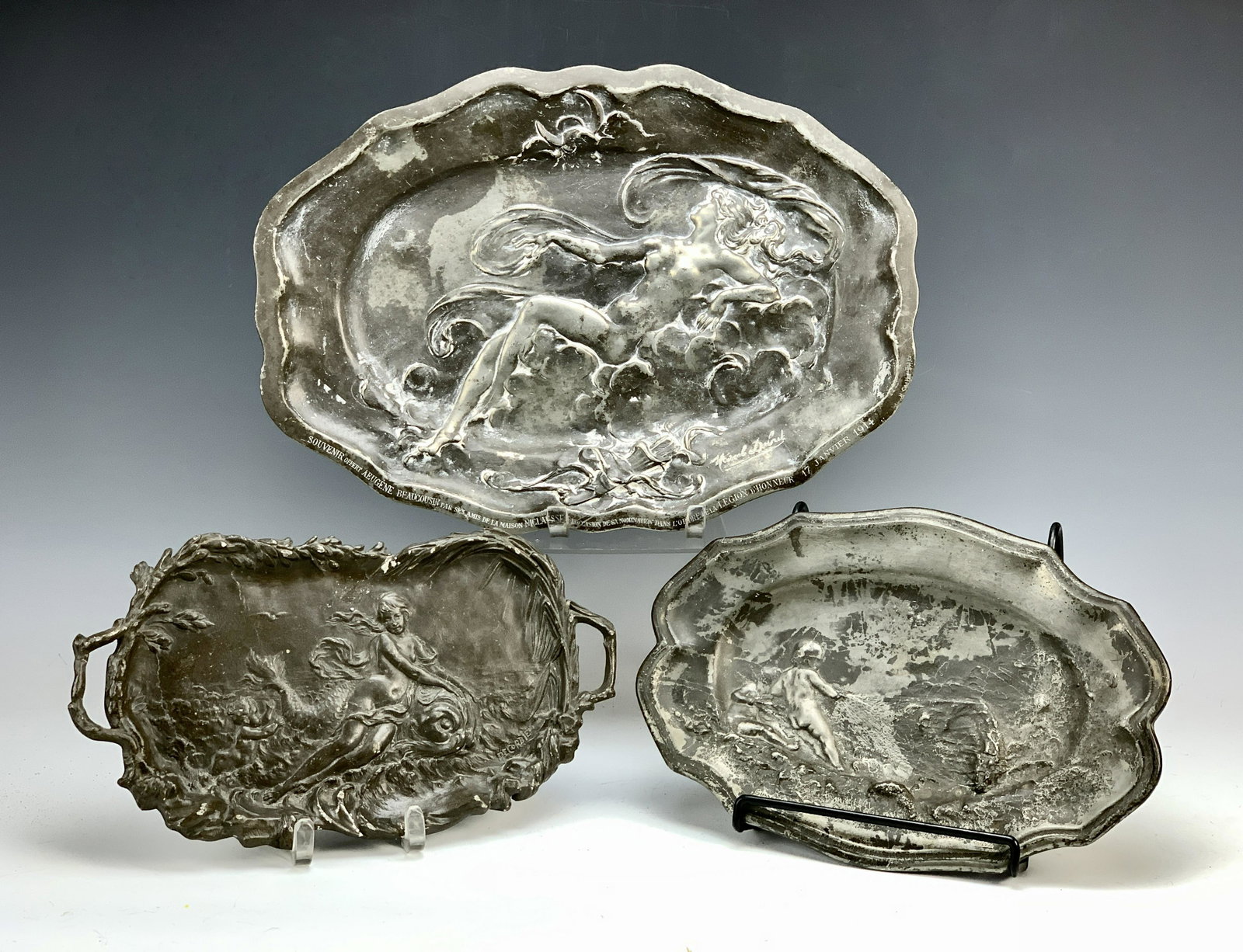 3 Art Nouveau Pewter Trays, Debut & Ledru: Circa 1914. Consisting of: a smaller tray of a couple of putti pulling in a fishnet, marked Susse F Paris, E; and artist signed Ledru. The second tray is larger, depicting a raised nude lady in the cl