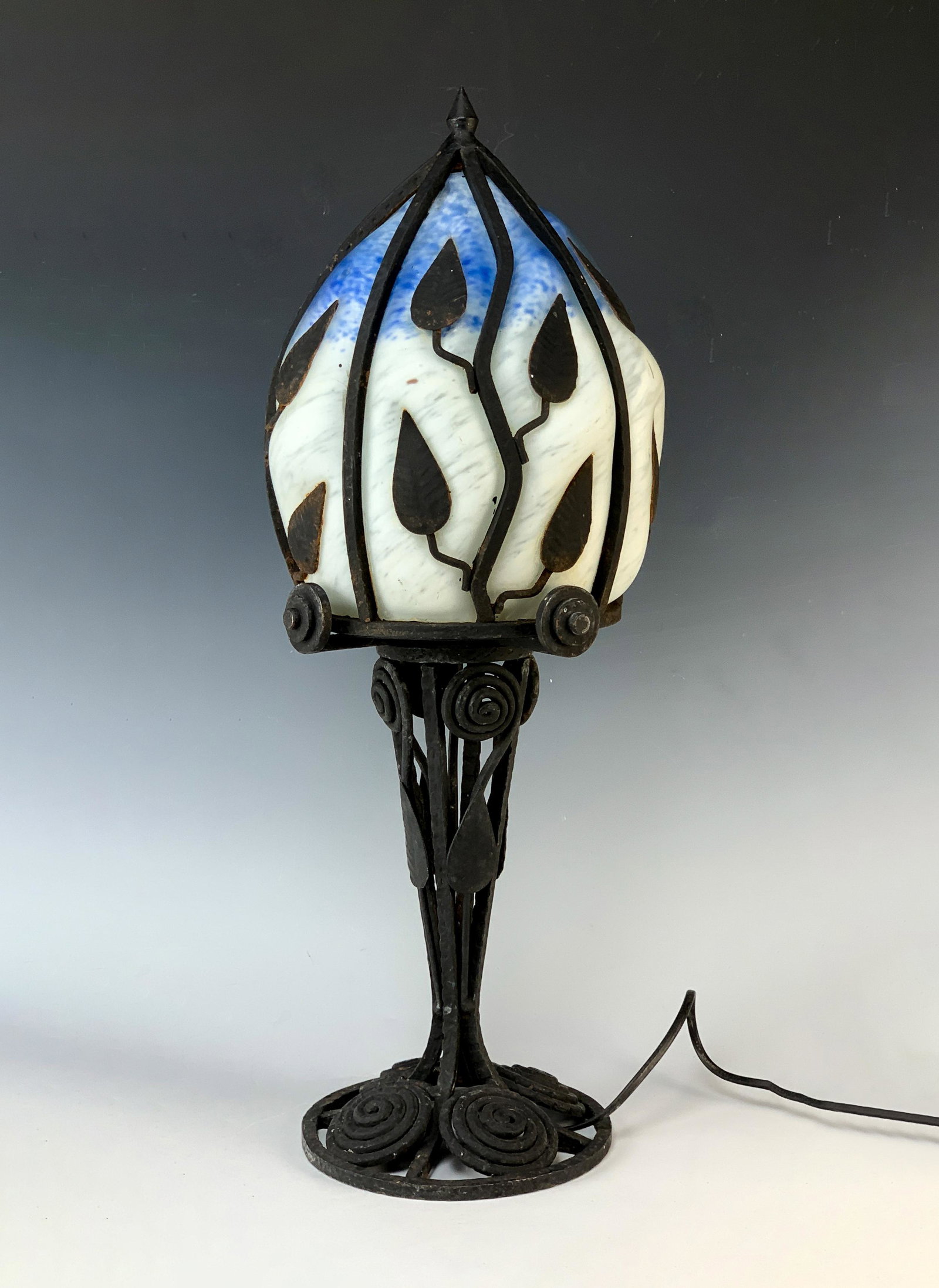 Art Deco Style Blow Out Glass & Iron Lamp: Unusual art deco style lamp having blue and white mottled glass blown into an iron frame, decorated with iron leaves and fancy iron matching base, 22" tall x 8" widest, in fine working order, very goo
