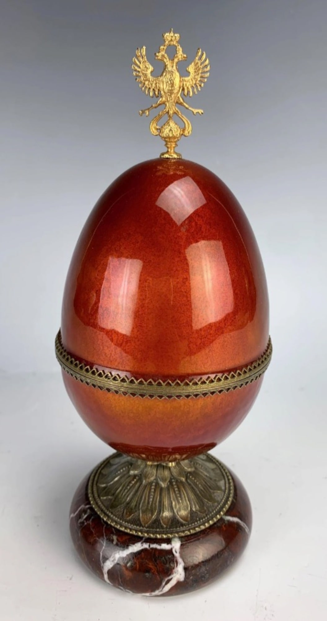 Russian Enamel Egg Box on Marble Base: Presenting a fine quality enameled red egg-shaped box adorned with a gilt bronze Fabergé-style double eagle finial. The interior is lined with red velvet and the box is mounted atop a Reuge marble ba