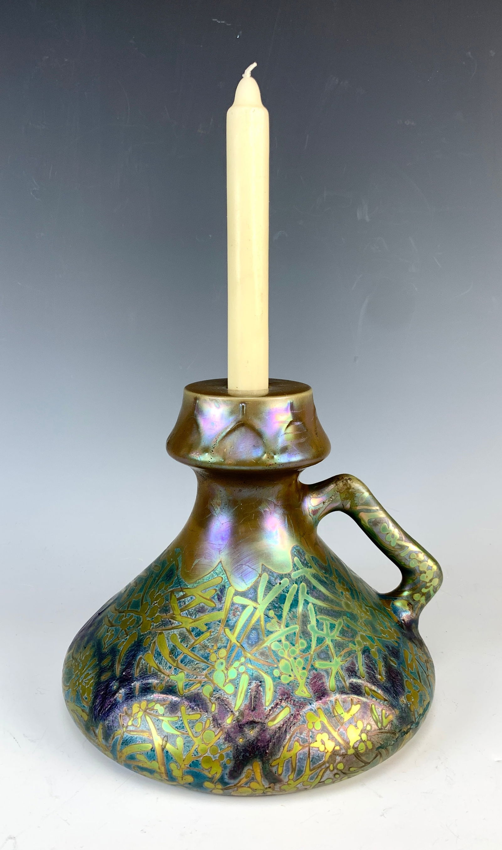 Clement Massier Iridescent Chamberstick C1900: Circa 1900. Beautiful Clement Massier iridescent chamberstick with leaves and flowers decor. Has a handle and candle holder. Signed on the bottom: Clement Massier, Golfe-Juan AM. Size: 8" tall x 9" wi