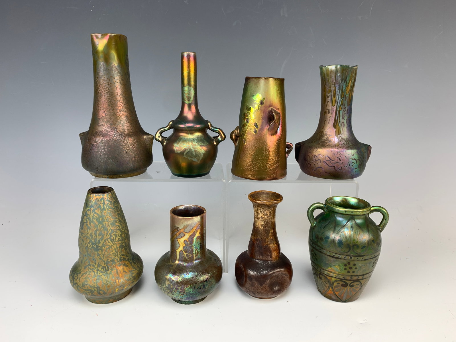 8 Massier & Others Iridescent Miniature Vases: Circa 1920s. A collection of 8 great assorted small iridescent vases. The lot includes 2 Clement Massier, 1 Delphin Massier, and 5 unsigned pieces. The tallest vase measures 5.5". Condition: overall g