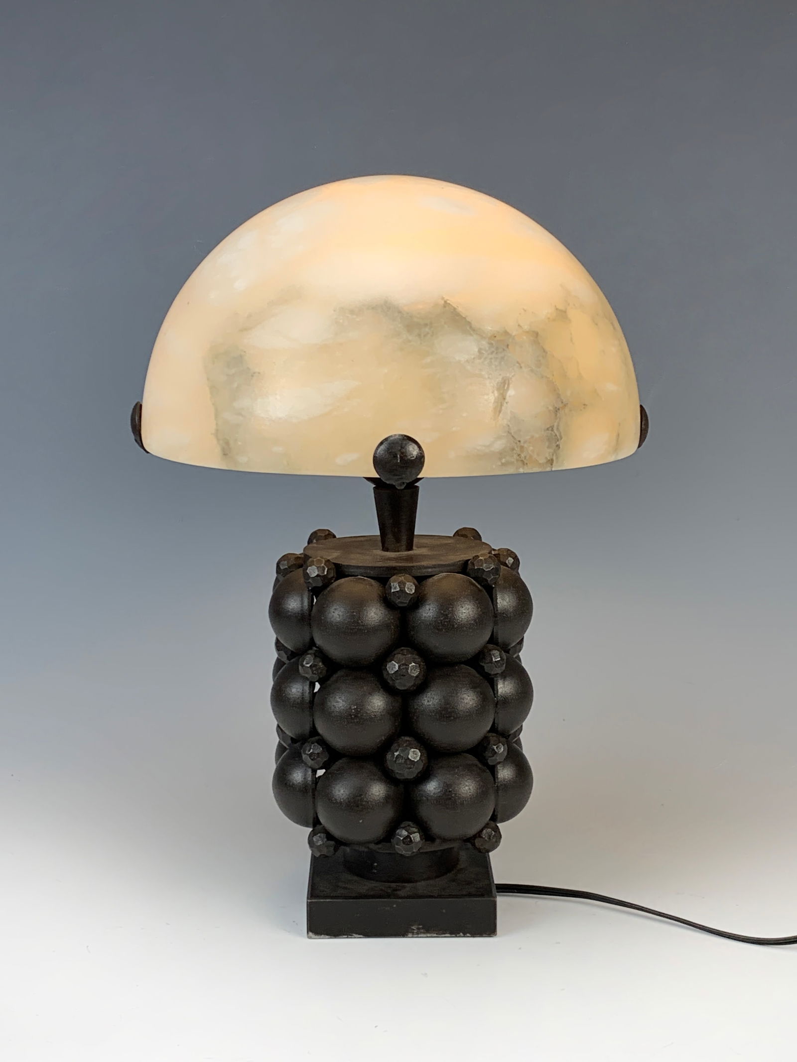Edgar Brandt (1880-1960) Iron&Alabaster Lamp: A wrought iron lamp base decorated with half spheres alternating with faceted balls in three rows. It is marked "E Brandt" on the square base. The lamp comes with an alabaster mushroom shade shaped as