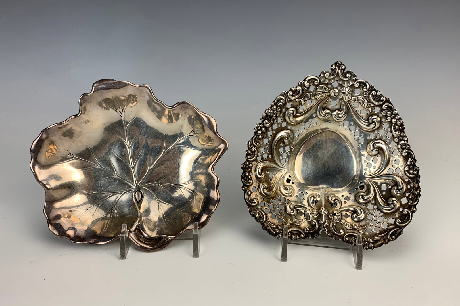 Two Sterling Silver Nut Dishes Heart&Leaf: Set of two sterling silver nut dishes. One is shaped with a pierced heart design decorated with ribbons and an ornate design, sitting on three ball feet, marked with Gorham silver mark. The second ste