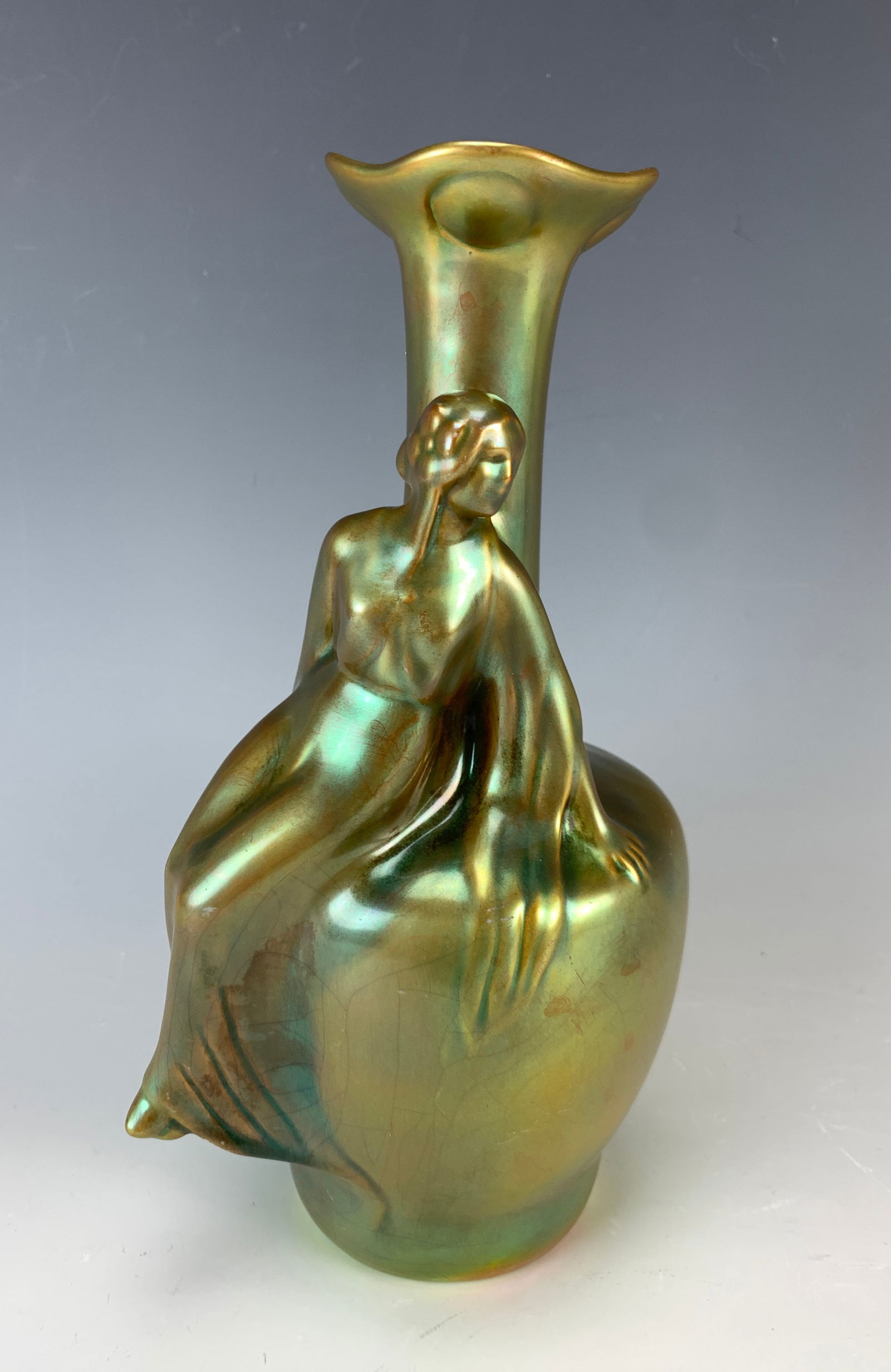 Signed Zsolnay Figural Lady Sitting On Vase: Having a gold iridescent glaze, marked with the Zsolnay logo. 9.25" tall. Condition: Good.