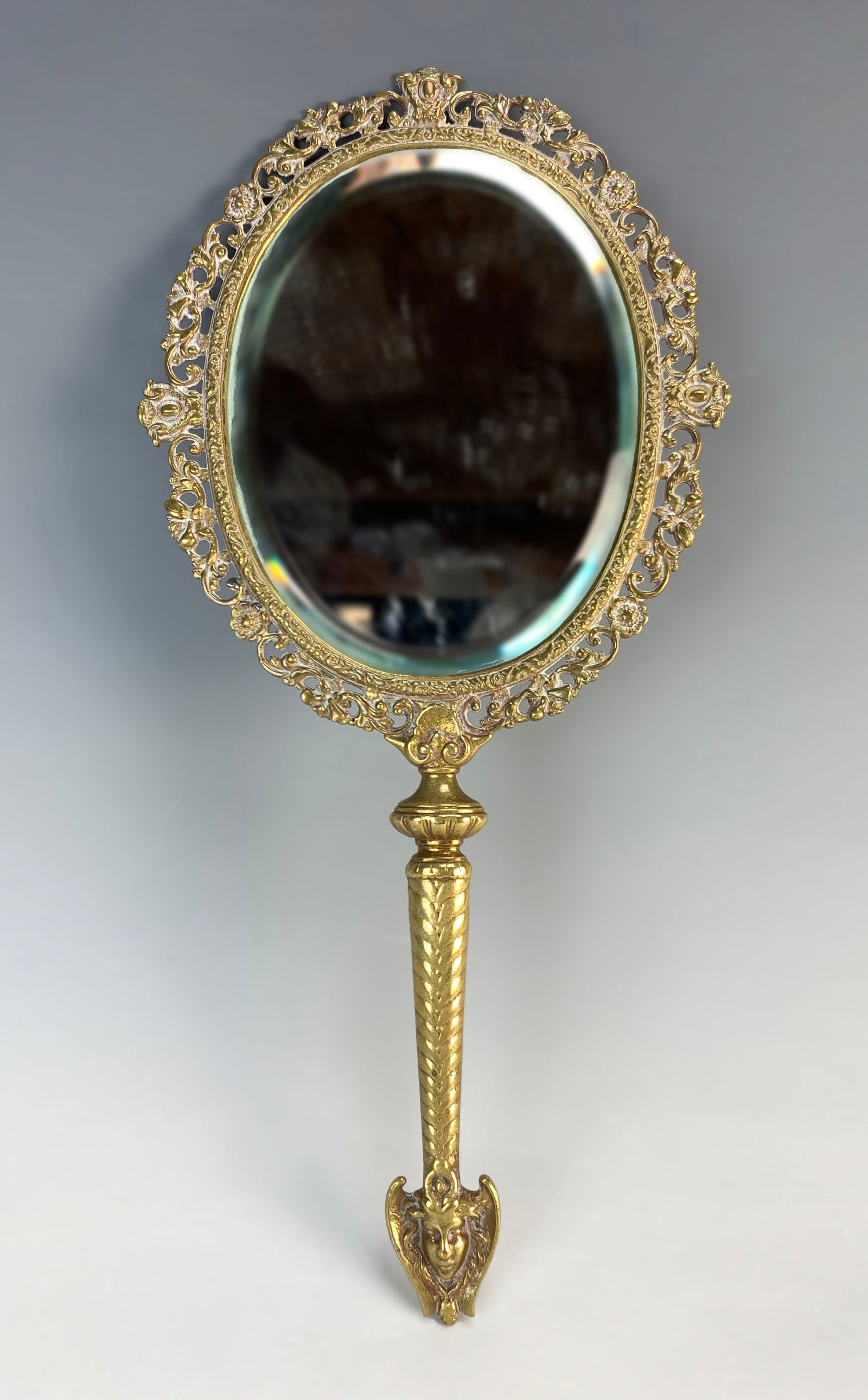 Tiffany & Co. Bronze Gilt Hand Mirror: Hand mirror in gilt bronze. Base of handle has a face of a woman. Mirror is beveled. Marked Tiffany & Co. Makers 6502/9962 "M". Size: 12" tall. Condition: Normal wear from age.
