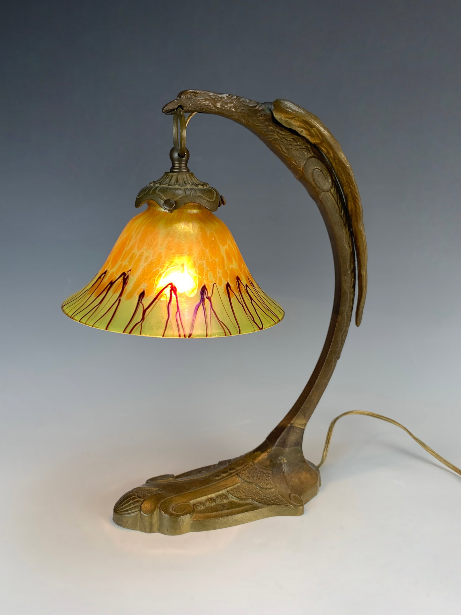 Bronze Eagle Desk Lamp with Loetz Shade: Circa 1910. Bronze lamp with an eagle holding a Loetz shade. Size: 14" tall. Condition: Good.
