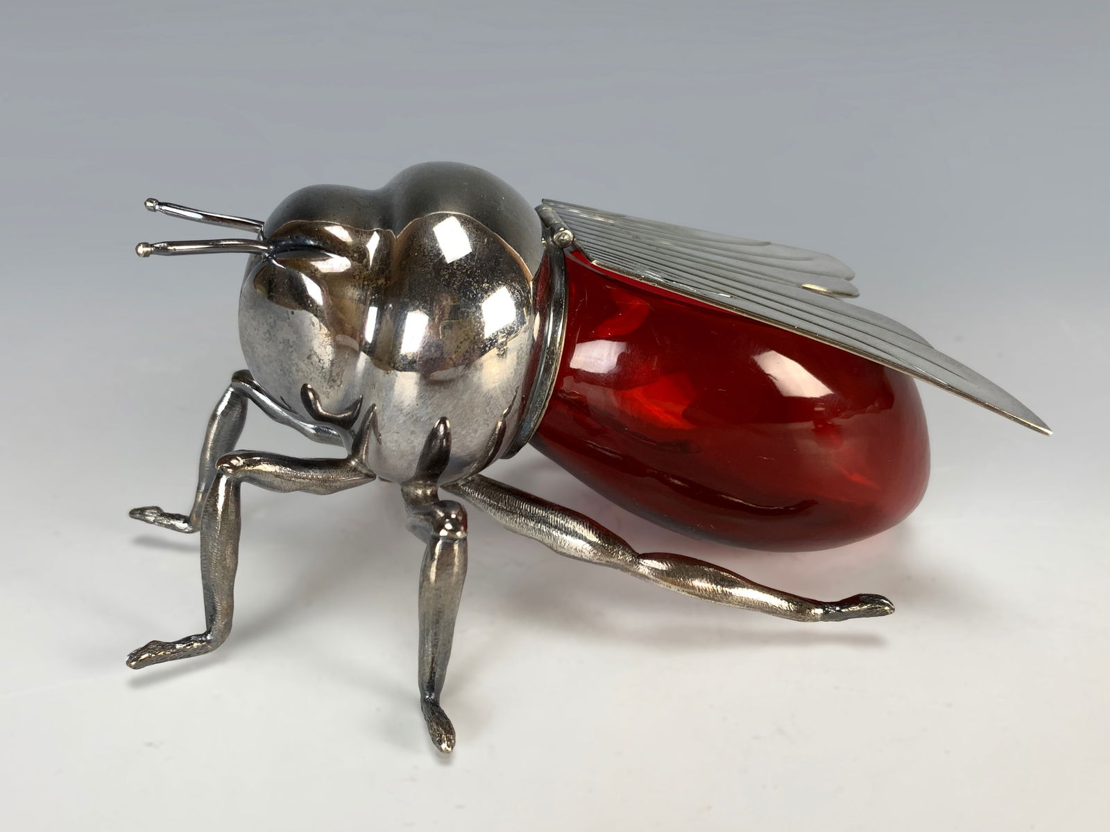Cranberry Glass Bumble Bee Honey Pot: Cranberry glass bumble bee honey pot with silver-plated bee lid in the form of an insect. The oval body has insect-themed old mounts, with the hinge cast depicting wings. Signed Mappin & Webb, London.